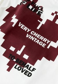Bawełniana koszulka z białą podstawą i bordowym wzorem graficznym. Tekst brzmi: "PEŁNE ŻYCIA", "BARDZO WIŚNIOWA RETRO" i "BYĆ KOCHANYM".