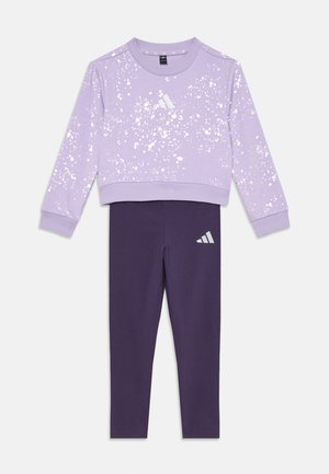 Sweatshirt lilas avec un motif de taches blanches, poignets côtelés, et un ensemble de leggings violets présentant un logo Adidas réfléchissant sur la cuisse.