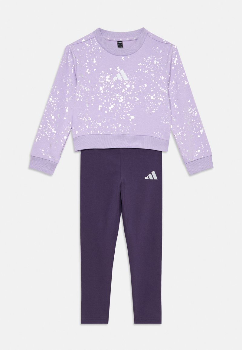 Felpa lilla con design a macchie bianche, polsini a coste e un set di leggings viola con un logo Adidas riflettente sulla coscia.