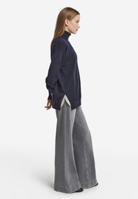 Marinblå polotröja med sidospjäll, kombinerad med gråa vida jeansbyxor, som visar en avslappnad passform och mjuk textur.