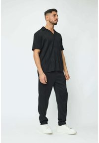 Chemise noire à manches courtes avec un motif de vagues texturé, associée à un pantalon noir assorti. Des baskets blanches complètent la tenue.