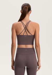 Fialová športová podprsenka s prekríženými ramienkami na chrbte, v kombinácii s príslušnými vysoko pásovými legínami, ktoré majú hladkú a elastickú textúru.
