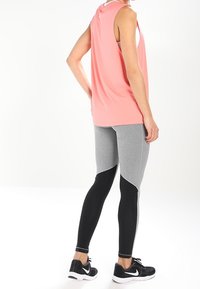 Top senza maniche rosa, leggings grigi e neri con accenti testurizzati e scarpe sportive nere. Focalizzato su materiali che offrono comfort e prestazioni.