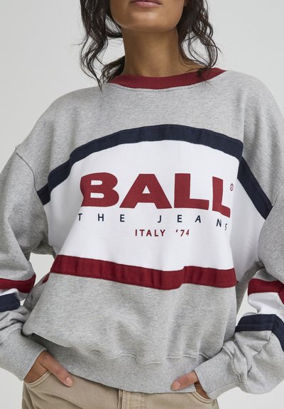 Sweat-shirt gris à col rond, avec de larges bandes rouges et bleu marine. Grand texte "BALL THE JEANS ITALY '74" affiché de manière proéminente.