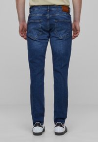 Temno modri traper hlače s slim fit krojem, z običajnimi zadnjimi žepi in usnjenim obližem na pasu. Klasična zasnova s petimi žepi.