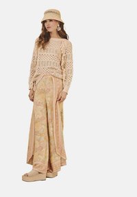 Suéter beige de ganchillo, pantalones de pierna ancha con estampado floral en tonos pastel y sandalias de plataforma. Completado con un sombrero tipo cubo a juego.