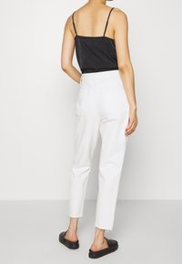 Černý top na tenkých ramínkách, bílé vysoce pasové tapered džíny s třepeným lemem a černé nazouvací sandály. Pohled ze zadu na outfit.