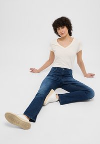 Camiseta blanca de cuello en v combinada con jeans de campana de color azul oscuro y zapatillas blancas. El tejido parece suave con un diseño mínimo.