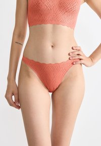 Koraalkleurige kanten bralette en thong set met een gemêleerd patroon en geschulpte randen, die een zachte, naadloze uitstraling benadrukken.