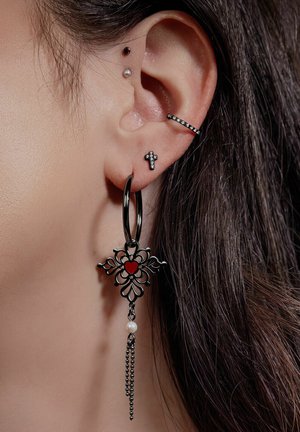 Schwarze Metall-Creole mit floralen Motiven und einem roten Herzakzent. Enthält eine hängende Kette mit einer Perlen-Applikation. Mehrere Ohrlöcher.
