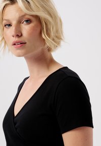 Sort tætsiddende t-shirt med v-udskæring og korte ærmer, lavet af ribbet stof, der viser en glat tekstur.