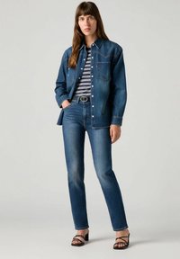 Denimtakki raidallisen paidan päällä, yhdistettynä korkea vyötäröinen sinisiin farkkuihin. Sisältää klassista ompelua, taskuja ja avoimen kauluksen. Mustat sandaalit.
