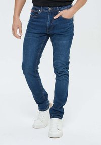 Jeans en denim slim fit bleu foncé avec une texture lisse, présentant un design traditionnel à cinq poches et de subtils détails de couture.