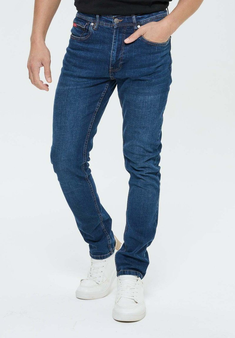 Jeans en denim slim fit bleu foncé avec une texture lisse, présentant un design traditionnel à cinq poches et de subtils détails de couture.
