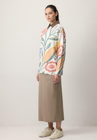 Suéter de punto con patrón floral multicolor en tela suave, combinado con una falda midi beige y zapatillas blancas, sobre un fondo liso.