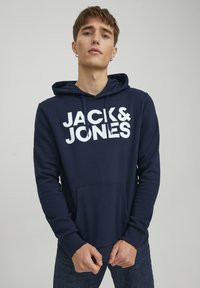 Navy blue hoodie made of cotton blend. White text "JACK & JONES" on front, featuring a kangaroo pocket and adjustable drawstring hood.