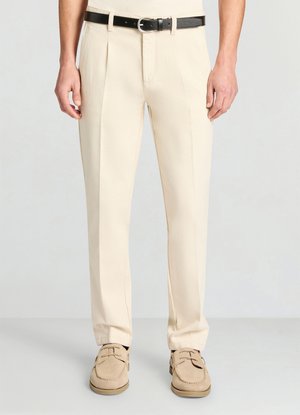 Beige Hose mit maßgeschneidertem Design, vorne plissiert und mit einem schwarzen Ledergürtel. Glatte Textur und gerade geschnittener Beinverlauf, kombiniert mit beigen Schuhen.