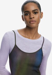 Gestapelte Outfit bestehend aus einem helllila, gerippten Langarmoberteil und einem durchsichtigen, dunklen, irisierenden Unterkleid mit dünnen Trägern.