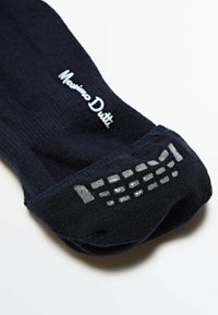 Chaussette noire en coton avec un design à côtes, un logo blanc et des points en caoutchouc gris texturé pour une meilleure adhérence sur la semelle.