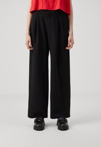 Black wide-leg trousers with pleats, made from smooth fabric. Styled with a red cropped top and black chunky shoes.