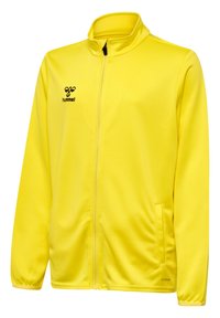 Geel zip-up jack van zacht materiaal, met zijzakken, een hoge kraag en een zwart logo op de borst.
