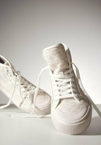 Białe sneakersy wysokie, wykonane z teksturowanej tkaniny, z wzorzystym deseniem, okrągłym noskiem, płaską podeszwą i białymi sznurówkami.