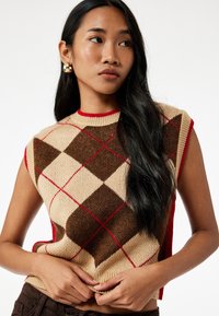 Ärmelloser Strickpullover mit einem beigen und braunen Argyle-Muster sowie roten Akzenten. Gerippter Rundhalsausschnitt und strukturierter Stoff.