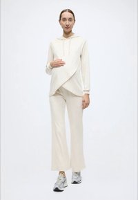 Σετ εγκυμοσύνης σε κρεμ απόχρωση, που περιλαμβάνει ένα κουκούλα κορυφή με σχεδιασμό draped και ταιριαστό παντελόνι με φαρδύ πόδι. Μαλακή υφή υφάσματος, άνετη εφαρμογή.