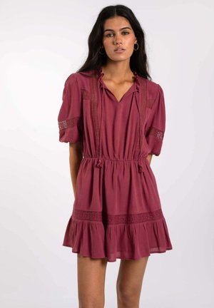 Robe bordeaux avec un décolleté en V, de courtes manches bouffantes, des accents en dentelle et une taille élastique. Elle présente un ourlet à volants en étage et un tissu texturé.