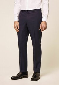 Mornarska odijela od glatkog materijala, sa uskim krojem, petljama za remen i krojem po mjeri, u kombinaciji sa crnim kožnim cipelama.