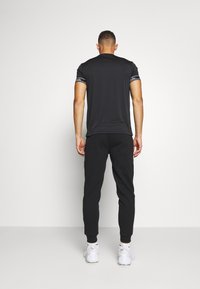 Black athletic t-shirt with short sleeves and white striping on cuffs, paired with black joggers and white sneakers. Minimalist design.