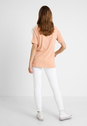 T-shirt di cotone rosa con maniche corte e dettagli bianchi sulle spalle, abbinato a leggings bianchi e sneakers alte grigio chiaro.