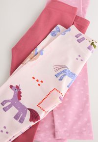 Drei Kinderleggings: ein einfarbiges pink, eines hellrosa mit Punkten und eines gemustert mit bunten Einhörnern und Formen.