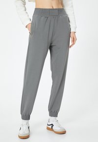 Grijze sweatpants gemaakt van zachte stof met een gerimpelde tailleband, taps toelopende manchetten en zijzakken, aangevuld met witte en grijze sneakers.