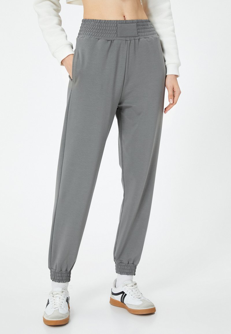 Grijze sweatpants gemaakt van zachte stof met een gerimpelde tailleband, taps toelopende manchetten en zijzakken, aangevuld met witte en grijze sneakers.