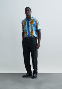 Short-sleeve shirt in blue with a multicolored map pattern; black trousers; glossy black shoes. Smooth fabric with a relaxed fit.