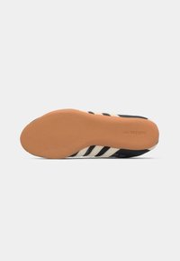 Black and white athletic shoe with three black stripes, rubber sole, and a textured, cushioned underside. Simple design with no notable accents.