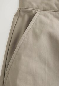 Gros plan sur un tissu beige avec des détails de coutures diagonales et une couture pliée, suggérant une poche sur un vêtement.