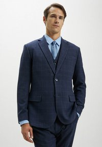 Jacket da suit a quadri blu navy con rever a pantaloni, chiusura a un bottone e due tasche frontali, abbinato a una camicia azzurra e una cravatta.