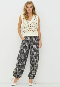 Tejszínszínű horgolt mellény virágmintával, szürke és rózsaszín árnyalatú mintás, bő szabású cargo nadrággal, húzózsinóros mandzsettákkal befejezve.