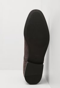 Chaussure en daim marron avec une semelle en caoutchouc texturée. Le talon est légèrement relevé et le bord présente une couture pour plus de durabilité.