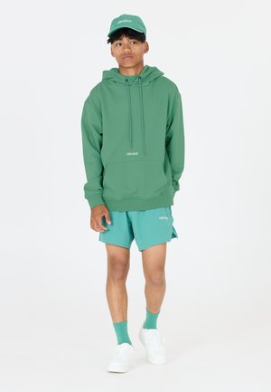 Grön huvtröja med snoddar, matchad med turkosa shorts, matchande strumpor och vita sneakers. Logotypen "LES ARCS" på båda.