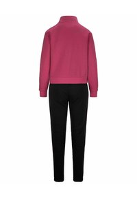 Sudadera rosa con cuello alto, combinada con pantalones negros. El material parece suave con una textura lisa y elementos de diseño mínimos.
