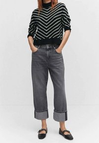 Un pull en maille noir et blanc à rayures avec un col rond, associé à un jean large à revers gris et des ballerines noires.