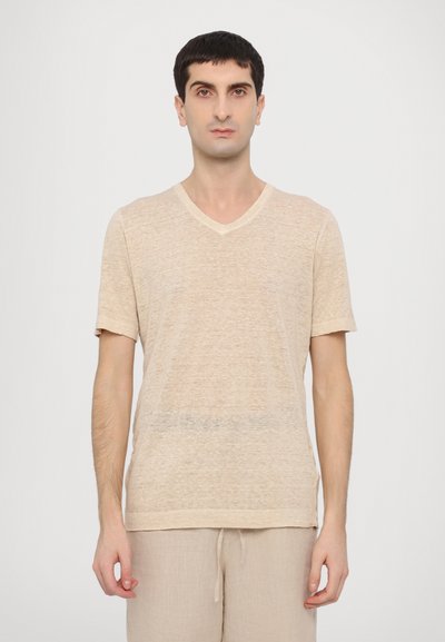 Beige V-Ausschnitt-T-Shirt aus leichtem, strukturiertem Stoff, mit kurzen Ärmeln und lockerer Passform. Kombiniert mit beigen Shorts.