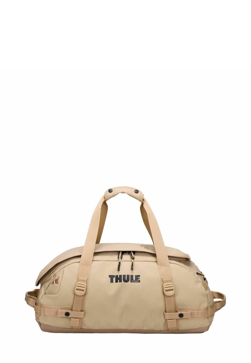 Sac de voyage beige avec une texture lisse, un design robuste, des poignées ergonomiques doubles et une poche zippée à l'avant ; arborant le logo Thule.