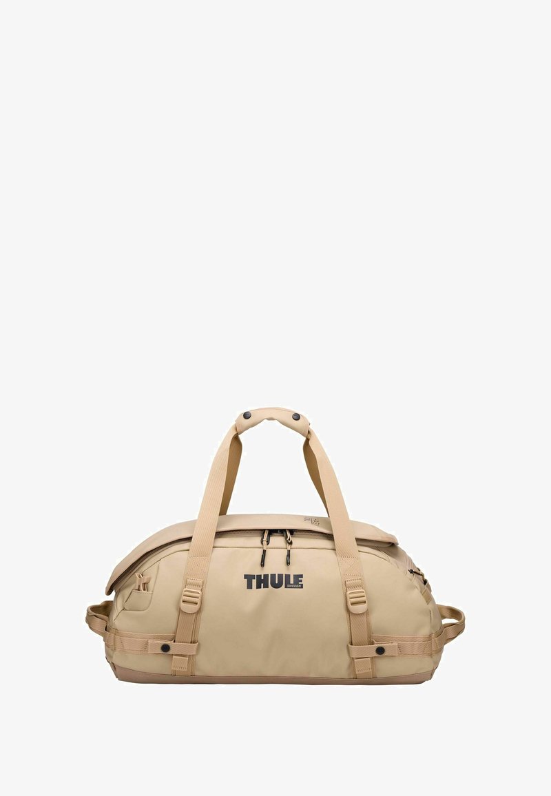 Sac de voyage beige avec une texture lisse, un design robuste, des poignées ergonomiques doubles et une poche zippée à l'avant ; arborant le logo Thule.