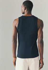 Navyblaues, geripptes Tanktop, taillierte Passform, mit rundem Halsausschnitt und schmalen Trägern, kombiniert mit hellcremefarbenen Hosen.