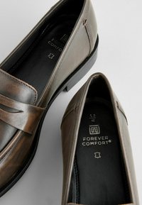 Loafers din piele maro cu o finisare netedă, având un design cusut pe partea superioară și o talpă interioară moale pentru confort.