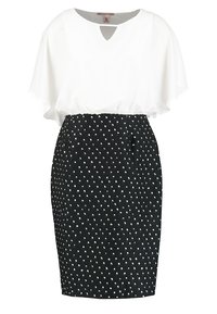Top bianco con scollo a V, maniche fluide e gonna a tubo nera con piccoli pois bianchi. Tessuto morbido, vestibilità su misura.